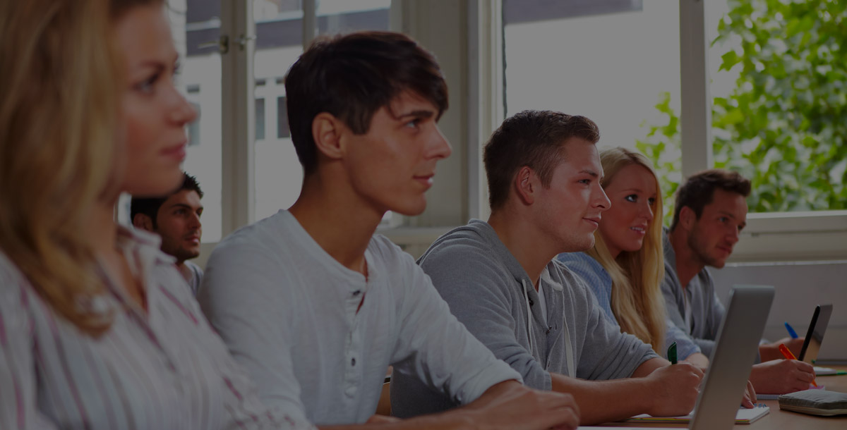 Young college students sitting in class utilizing multiple electronic devices