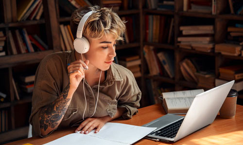 Young student studying in a library using audio to aid in learning
