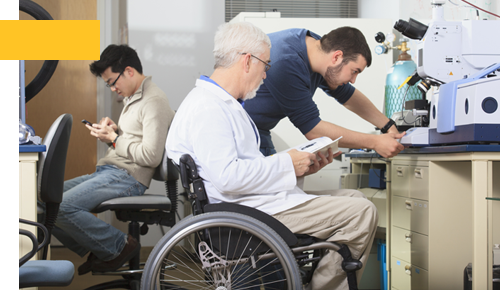 Professor with muscular dystrophy and engineering student using manual to adjust x-ray fluorescence analyzer in a laboratory