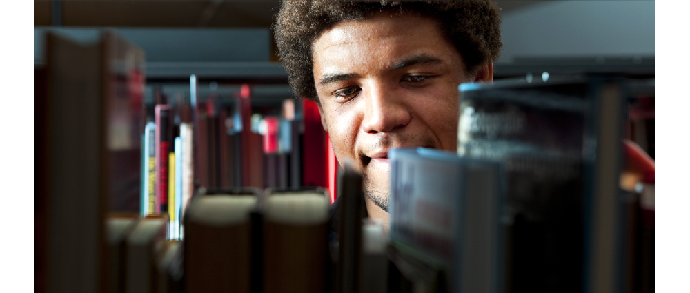 Male student browsing books in university library stacks